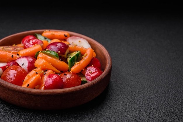 Délicieuse salade juteuse fraîche avec des radis, des tomates, des carottes, des concombres, des épices et des herbes sur un fond de béton sombre.