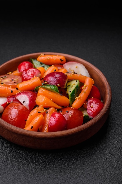 Délicieuse salade juteuse fraîche avec des radis, des tomates, des carottes, des concombres, des épices et des herbes sur un fond de béton sombre.