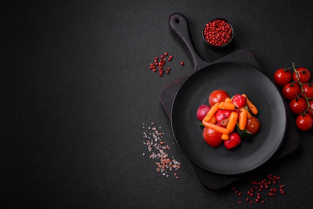 Délicieuse salade juteuse fraîche avec des radis, des tomates, des carottes, des concombres, des épices et des herbes sur un fond de béton sombre.