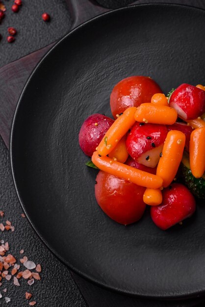 Délicieuse salade juteuse fraîche avec des radis, des tomates, des carottes, des concombres, des épices et des herbes sur un fond de béton sombre.