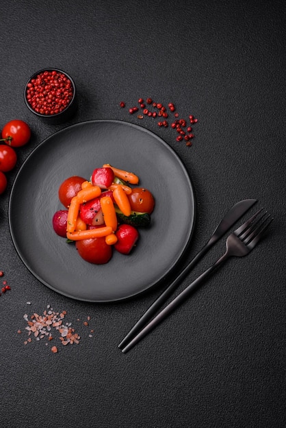 Délicieuse salade juteuse fraîche avec des radis, des tomates, des carottes, des concombres, des épices et des herbes sur un fond de béton sombre.