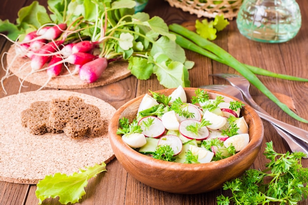 Délicieuse salade de légumes de printemps de concombre, radis, œufs de caille, verts et huile dans une assiette sur une table en bois