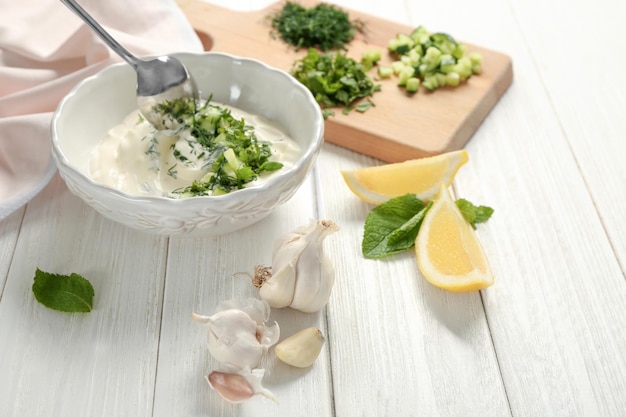 Délicieuse sauce au yaourt dans un bol avec des ingrédients sur fond de bois