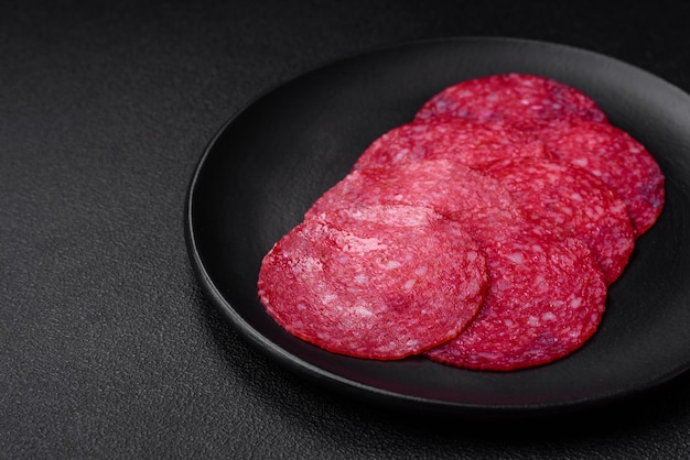 Délicieuse saucisse au salami fumé avec des épices salées et des herbes coupées en tranches sur un fond en béton sombre