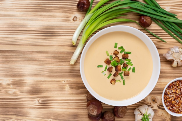 Délicieuse soupe aux marrons sur un espace en bois avec des assaisonnements et des oignons.