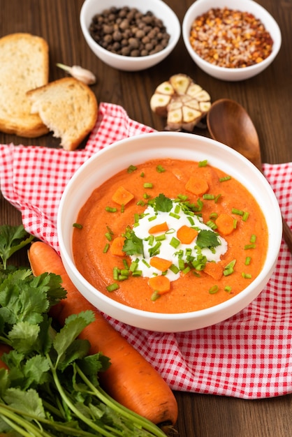 Délicieuse soupe de carottes traditionnelle aux herbes et crème sure sur une table en bois.