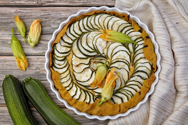 Délicieuse tarte aux courgettes maison avec du fromage blanc et des herbes entourées de graines de fleurs et de courgettes