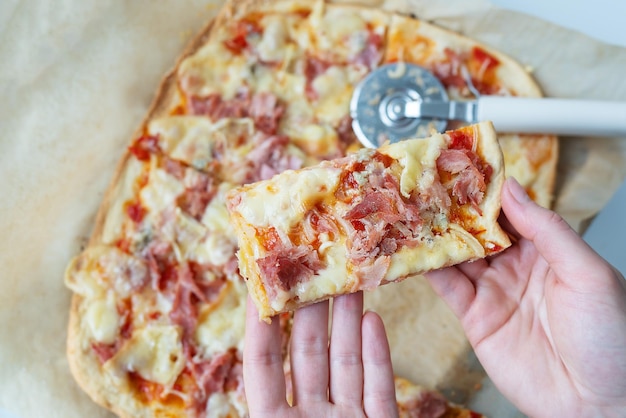 Délicieuse tranche de pizza juteuse avec jambon oignon et fromage Couteau à pizza sur le fond Cuisson de la pizza à la maison la jeune fille tient un morceau de pizza dans ses mains