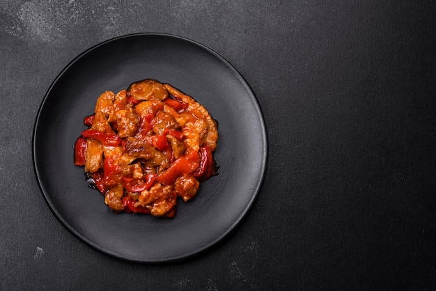 Délicieuse viande juteuse avec piments et sauce sur une plaque en céramique noire sur fond de béton foncé