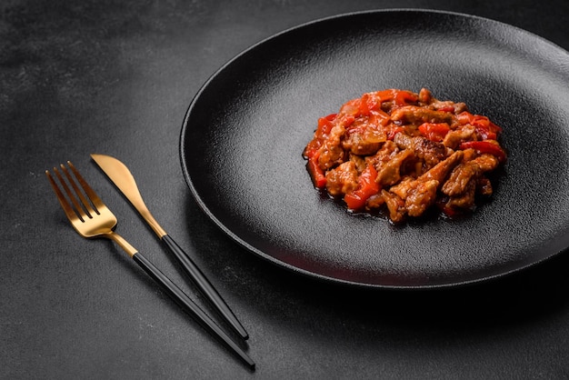 Délicieuse viande juteuse avec piments et sauce sur une plaque en céramique noire sur fond de béton foncé