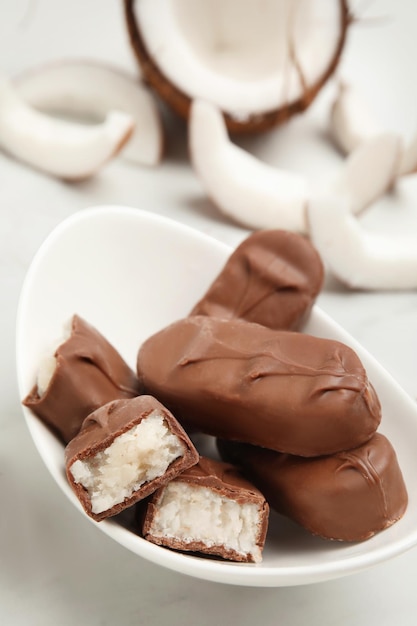 Délicieuses barres chocolatées au chocolat au lait avec remplissage de noix de coco dans un bol sur un gros plan de table blanc Espace pour le texte