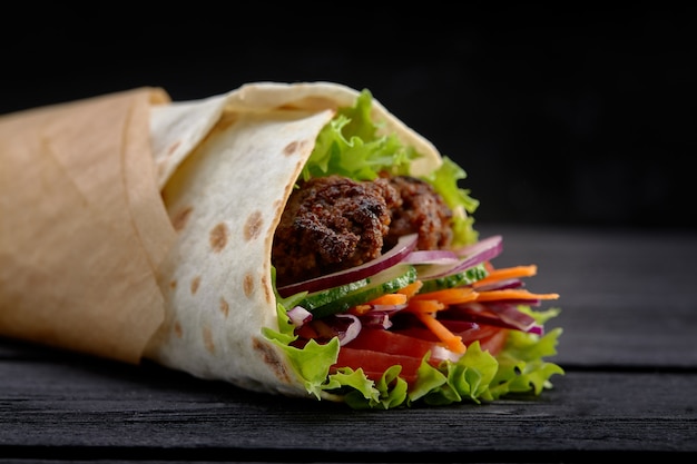 Délicieuses brochettes de doner avec des garnitures de salade fraîche et de la viande rôtie rasée servies dans des tortillas sur du papier brun comme collation à emporter