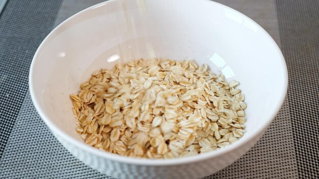 De délicieuses céréales de bouillie jaune tombent dans un bol en céramique blanche sur une table grise le matin en vue rapprochée extrême