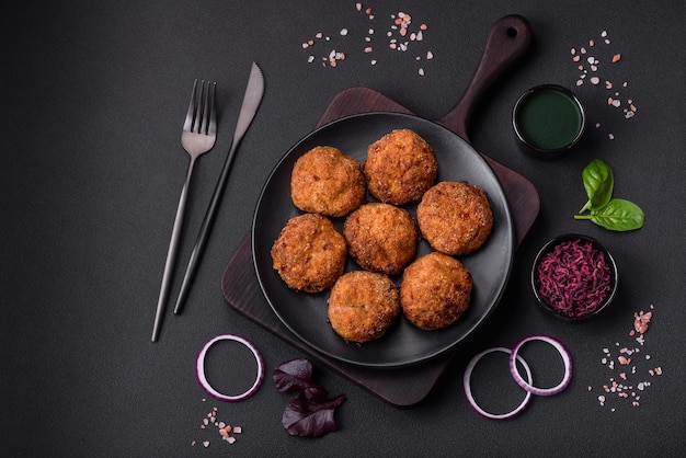 De délicieuses côtelettes de viande fraîche ou de légumes avec des épices et des herbes sur une plaque noire sur un fond de béton foncé