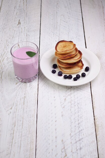 De délicieuses crêpes aux myrtilles et au yogourt aux myrtilles sur une table en bois clair avec des feuilles de menthe.