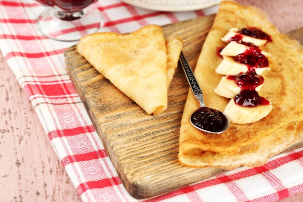 De délicieuses crêpes avec de la confiture de baies et des bananes sur planche de bois sur fond de bois