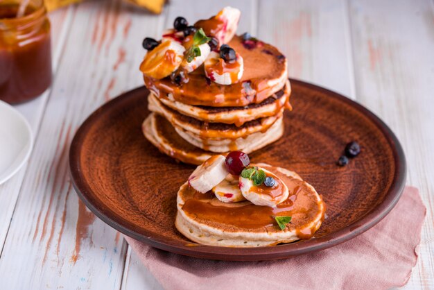 De délicieuses crêpes luxuriantes avec des fruits frais et des baies, servies avec du caramel salé. Menthe, thé, jus d'orange, lait sur la table.