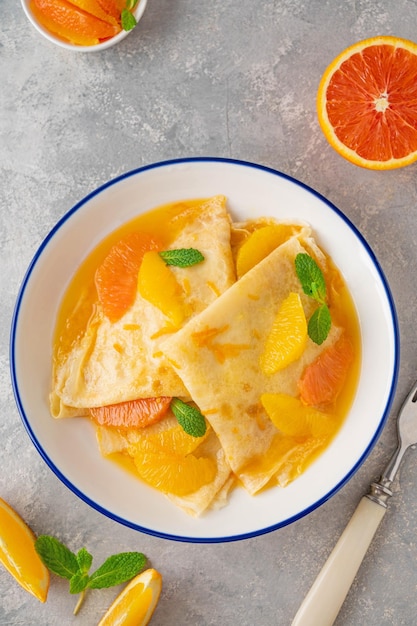 Délicieuses crêpes suzette au sirop d'orange et tranches de fruits sur fond de béton gris