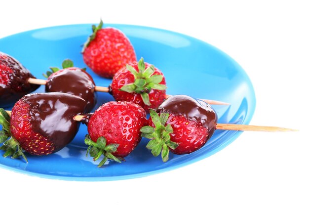 Délicieuses fraises au chocolat sur une plaque bleue isolée sur blanc