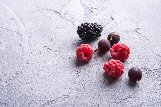 Délicieuses framboises mûres fraîches, mûres, groseilles à maquereau et groseilles rouges, fruits des aliments sains sur table en béton en pierre, vue d'angle macro copie espace