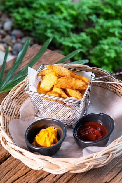 Photo de délicieuses frites, servies avec du ketchup et de la sauce à la moutarde. disposé dans un beau panier en rotin, posé sur une table en bois.