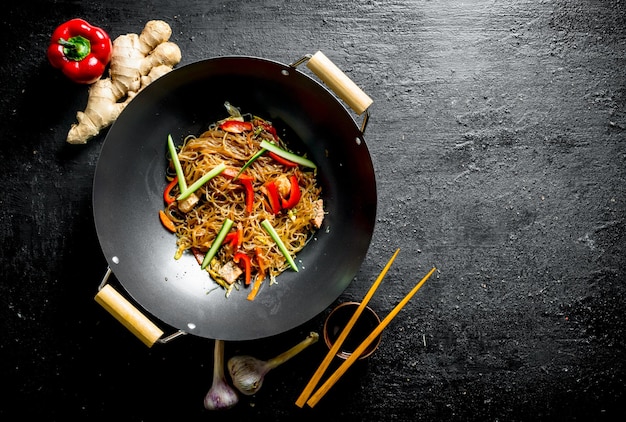 Photo délicieuses nouilles cellophane dans un wok de poêle avec des baguettes