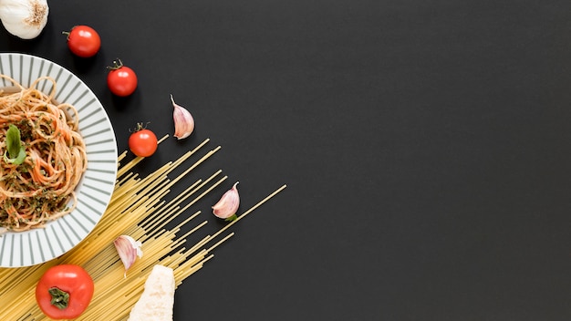 Photo délicieuses nouilles italiennes avec des spaghettis crus; tomate; gousses d'ail sur fond noir
