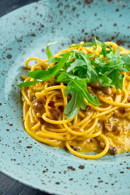 Délicieuses pâtes italiennes à la carbonara avec bacon et jaune cru, parmesan et roquette. Pâtes maison servies dans une assiette bleue sur une surface sombre