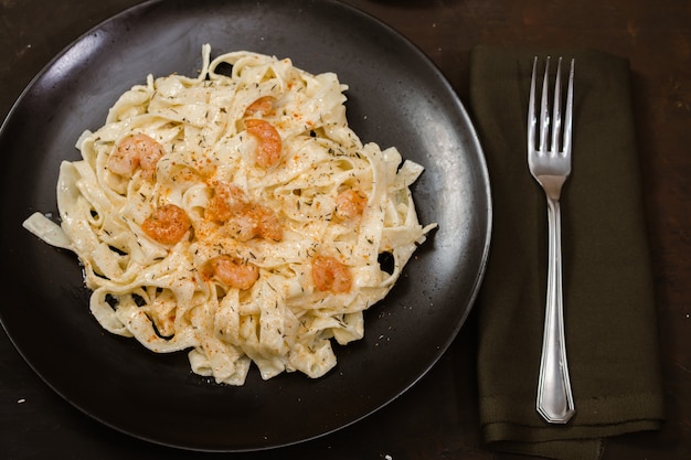 Délicieuses pâtes italiennes. Fetuccini aux crevettes et sauce aux herbes sur plaque noire et fond sombre.