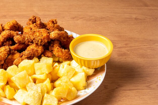 Délicieuses pépites de poulet avec frites et sauce piquante sur table en bois.