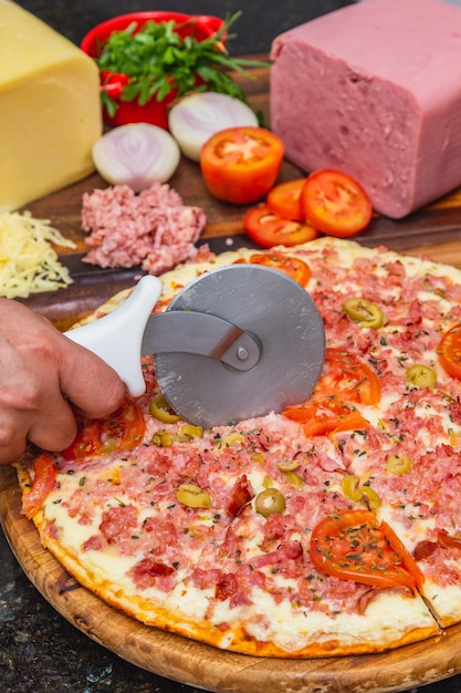 Photo de délicieuses pizzas au fromage et au jambon mélangées coupées prêtes à cuire des pizzas à la maison à côté d'une planche de bois avec des ingrédients