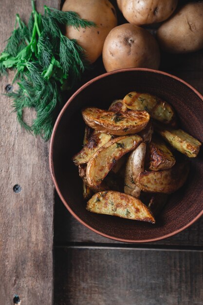 De délicieuses pommes de terre cuites au four dans un bol en terre avec des épices, de l'aneth et des oignons verts sur une table en bois, vue du dessus