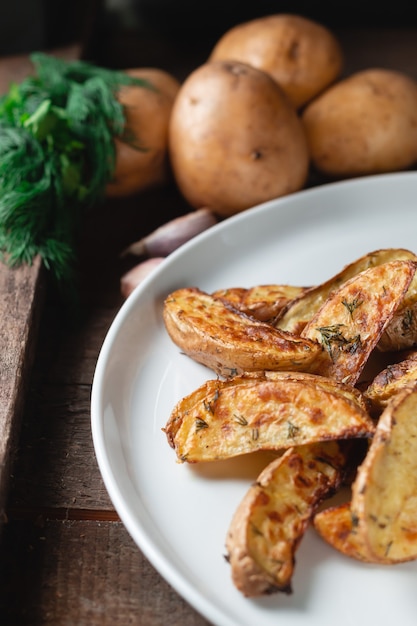 De délicieuses pommes de terre cuites au four dans une grande assiette blanche avec des épices, de l'aneth et des oignons verts sur une table en bois