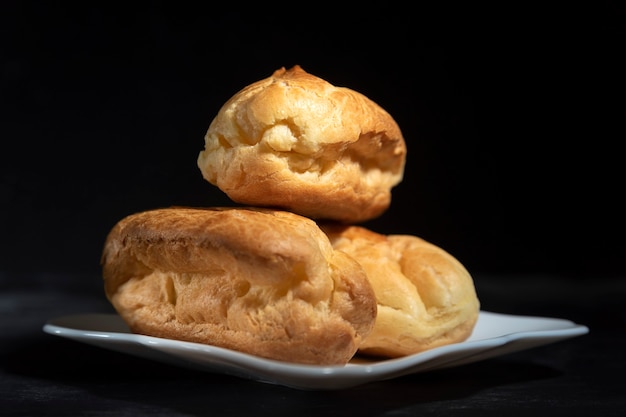 Délicieuses profiteroles ou éclairs sans crème sur soucoupe. Fermer. Fond noir.