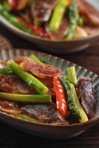 Délicieuses saucisses fumées chinoises sautées maison épicées aux asperges sur une table en bois sombre pour le repas.