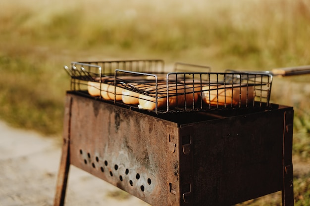 De délicieuses saucisses grillées reposant sur la grille de fer d'un barbecue portable sur des charbons ardents pendant qu'elles cuisent à la perfection