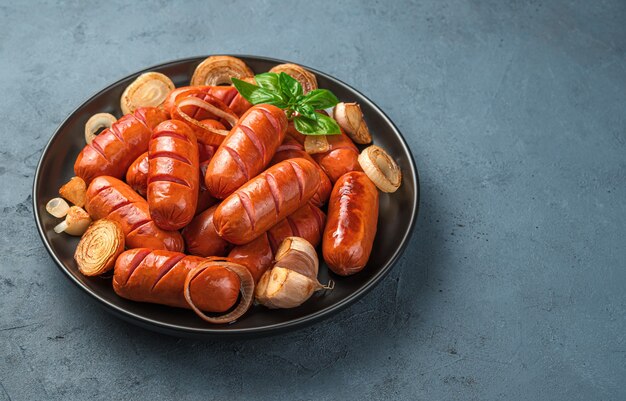 De délicieuses saucisses juteuses à l'ail et aux oignons dans une assiette noire sur fond gris-bleu. Vue latérale, espace de copie