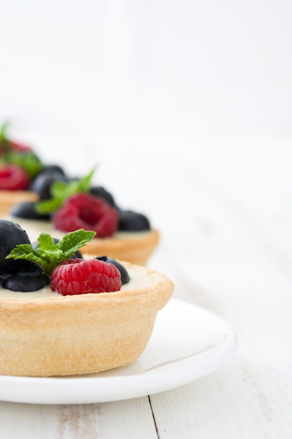 Délicieuses tartelettes aux framboises et bleuets sur table en bois blanc