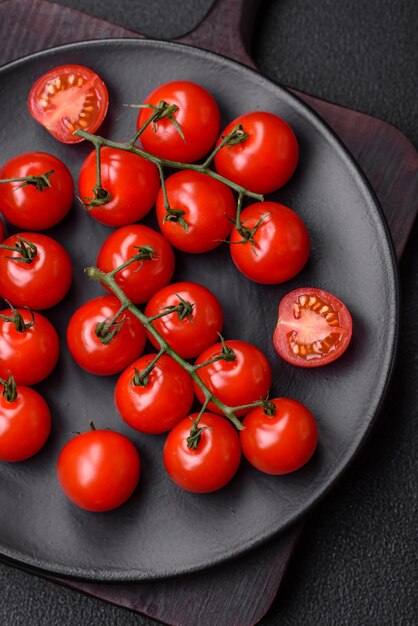 Délicieuses tomates cerises fraîches sur les branches comme ingrédient pour cuisiner un plat végétarien sur fond de béton foncé