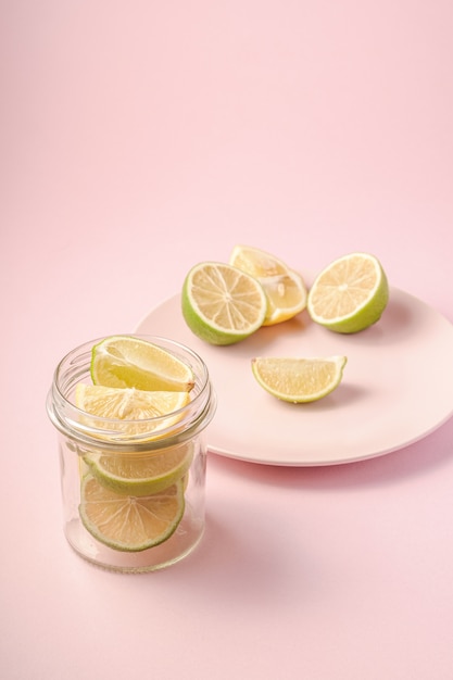 Délicieuses tranches d'agrumes au citron et au citron vert dans un bocal en verre près de la plaque rose avec des fruits