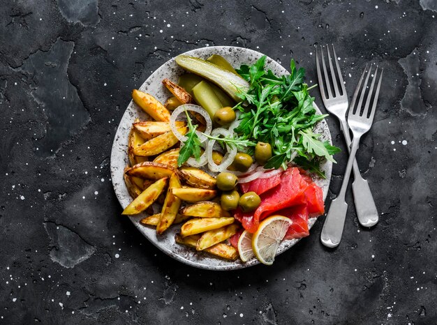 Délicieux apéritif assiette de tapas frites saumon roquette cornichons olives sur fond sombre vue de dessus