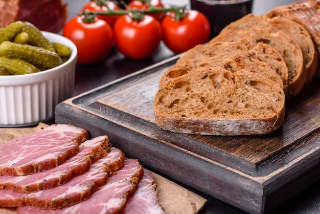 Délicieux bacon frais tranché avec du pain et des légumes sur un fond de béton foncé