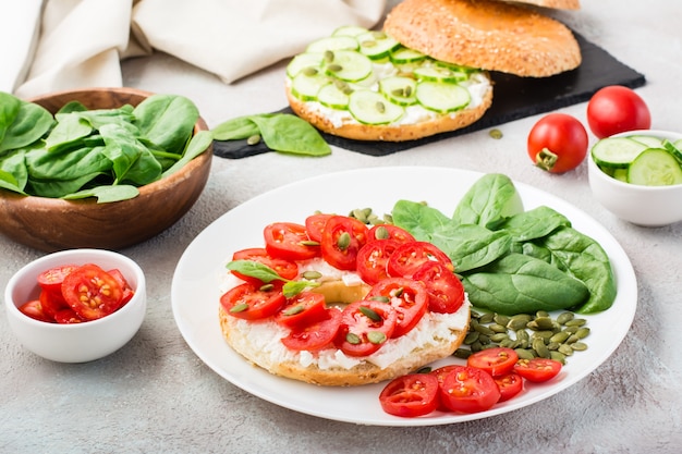 Délicieux bagel farci de feta, tomates et graines de citrouille et feuilles d'épinards sur une assiette. Snack vitaminé léger et sain