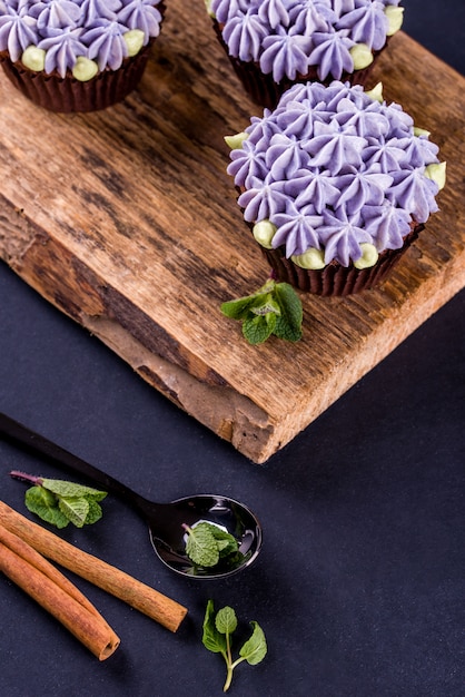 Délicieux et beaux cupcakes au chocolat avec de la crème, de la menthe, des bâtons de cannelle, du thé sur la table.