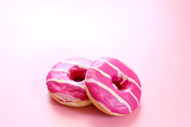 Délicieux beignet aux fraises. Donut cercle fait maison avec glaçage rose et rayures blanches sur le fond rose tendre à la mode