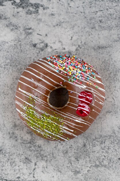 Délicieux beignet glacé au chocolat avec des paillettes sur fond de pierre.