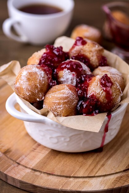 De délicieux beignets de fromage cottage faits maison dans du sucre en poudre avec de la confiture de baies sur fond de bois