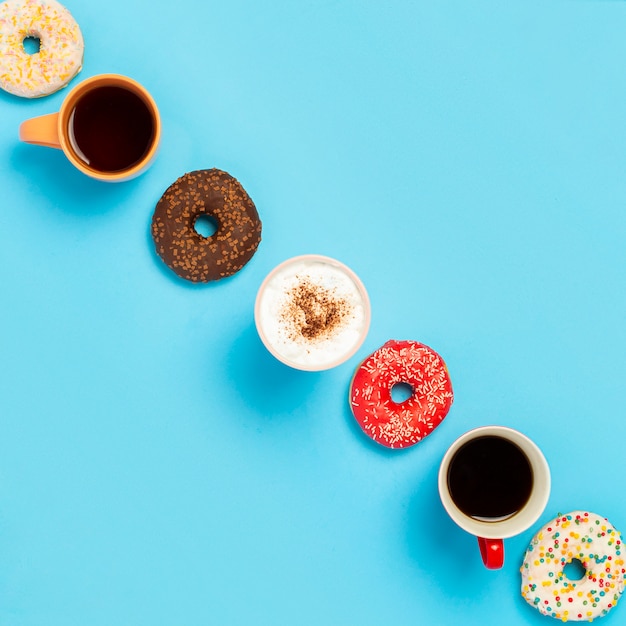 Délicieux beignets et tasses avec boissons chaudes, café, cappuccino, thé sur une surface bleue. Concept de bonbons, boulangerie, pâtisseries, café, réunion, amis, équipe amicale. Carré. Mise à plat, vue de dessus