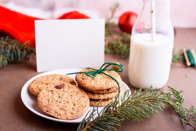 Délicieux biscuits au chocolat sur une assiette blanche, lait, bonnet de Noel, maquette pour le texte. Lettre et cookies pour le père Noël.