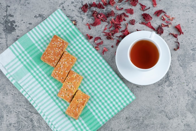 Délicieux biscuits aux graines de sésame et tasse de thé aromatique sur une surface en marbre.